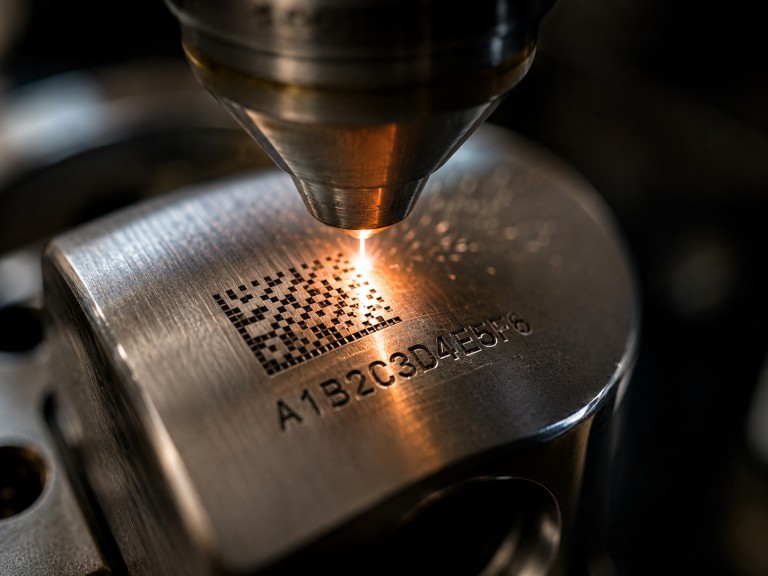 Close-up of fiber laser beam engraving high-contrast serial number and DataMatrix traceability code on polished stainless steel metal surface